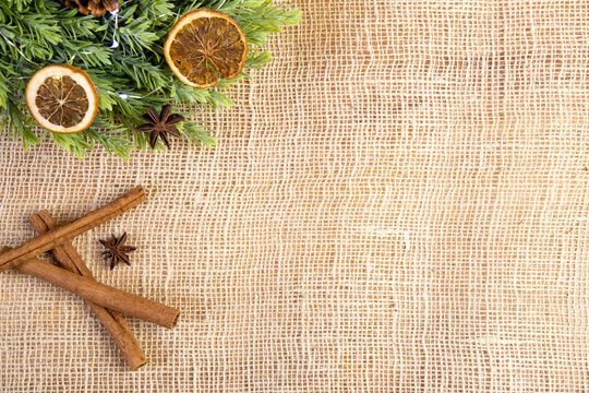 close-up of cinnamon sticks, anise, dry oragnes, green wreath and cone, bright organic, natural christmas decoration with food on jute background, raw ingredients, spices flat lay