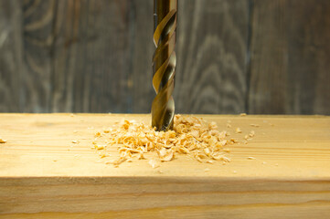 A drill for woodworking punches a hole in a wooden block with a lot of wood chips. Wood shavings...