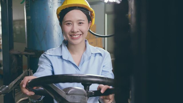 happiness smiling asian female woman worker in safty helmet driving forklift in warehouse factory
