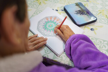 Mujer blanca de noventa años en confinamiento por coronavirus o covid-19, haciendo tareas de dibujo como entretenimiento.