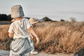 Naklejka na ściany i meble Two-year-old child in a hat walks along a country road, summer. Knowledge of the world.