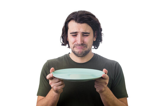 Desperate man crying as looks at an empty dish plate in his hands, isolated on white background. Dissatisfied guy weeping as has no food to eat. Global crisis and hunger issue. Famine and starvation