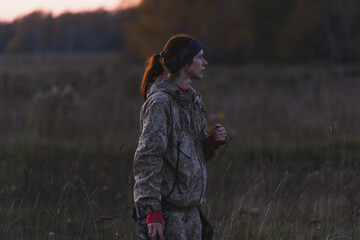 A girl in camouflage on a hunt walks across the field