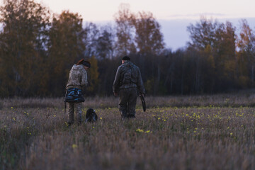 Hunters with guns go hunting. Two hunters cross the field into the forest in search of animals....