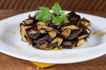 Plate of diced aubergines on a cream of yellow cherry tomatoes in a white plate. Wood background. Selective focus.