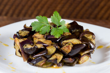 Plate of diced aubergines on a cream of yellow cherry tomatoes in a white plate. Wood background. Selective focus.