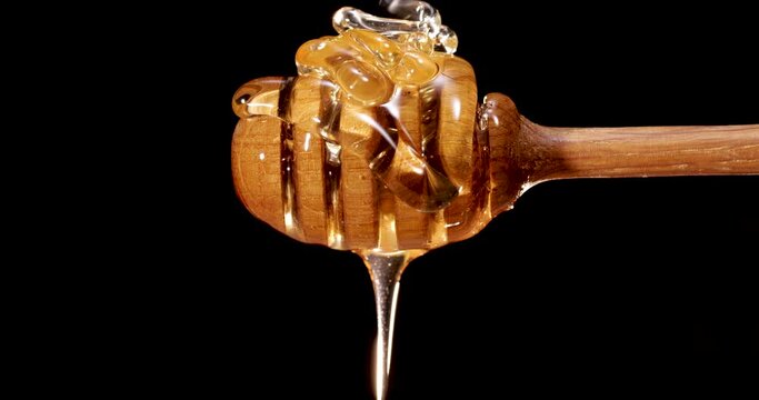 honey dripping from a wooden spoon on a black background