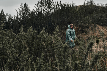Naklejka na ściany i meble A man in a green raincoat walks along a country road, cloudy, autumn.