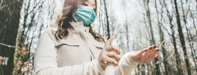Close-up portrait of nice attractive  girl wearing safety mask using disinfection spray in public park
