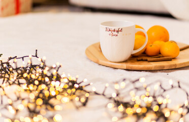 A white cup with the inscription Wonderful Winter stands on a wooden tray, pallesins and cinnamon lie next to it. The tray is on a soft white carpet.