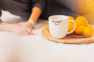 The girl lies on the carpet. Nearby is a wooden fruit tray and a large white cup