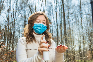 Close-up portrait of nice attractive  girl wearing safety mask using disinfection spray in public park