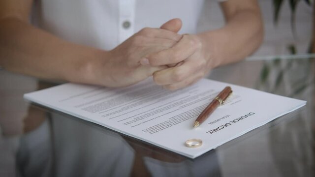 Divorce decree on the table. A view of a stressed woman's hand and a wadding ring on the table with divorce papers.