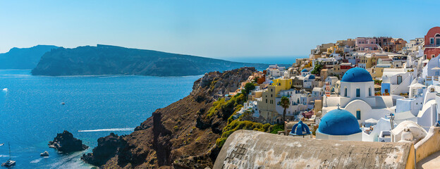 Naklejka premium A panorama view of the village of Oia, Santorini and the island of Thirasia in the background in summertime