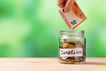 A woman puts ten euros in a jar for a donation close up.