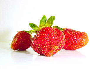 three berries Strawberries with leaves focus on the berry in the middle. Light background, healthy food concept