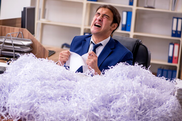 Young male employee and a lot of cut papers in the office