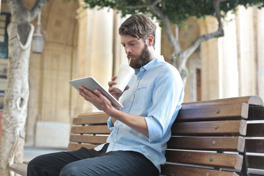 young man uses a tablet sitting on a bench