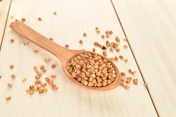 Not cooked organic buckwheat with a wooden spoon, close-up, on a white wooden table.