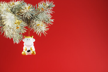 Figure of a Cow on a spruce branch, on a red background. Free space for text.
