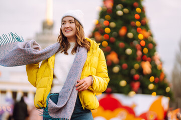 Young woman in warm winter clothing posing at festival street market near New year tree. Happy...