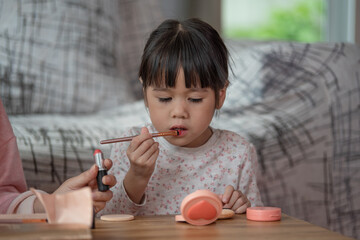Asian little girl trying use cosmetic by themselves, she use lipstick paint on her lips, make up artist