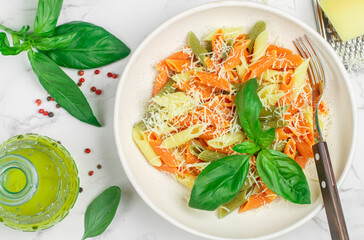 Tricolor pasta. Multicolored Penne (wheat, spinach, tomato) in a white plate with cheese, Basil and olive oil. Delicious Mediterranean dinner. Selective focus, top view