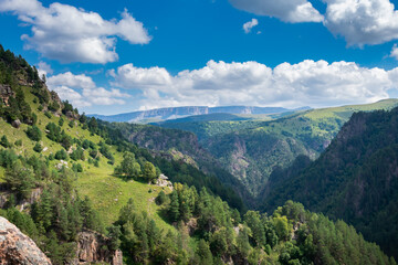 Obraz premium Beautiful landscape of mountainous woodlands and white clouds in the sun. Mountain ranges, top view, close-up. Mountain peak.