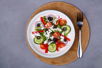Light plate of Greek salad on a round shelf with a fork on a concrete background.