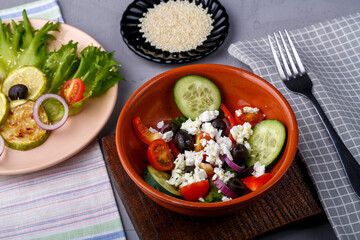 plate with grilled zucchini on lettuce leaves and greek salad on a gray background on a napkin with a fork