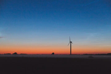 Obraz premium wind turbine at sunset and fog over a field