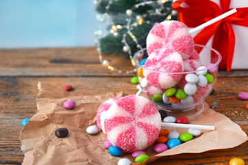 Peppermint striped candies with multicolored sweets over holiday background on wooden table. Christmas or new year traditional treat.
