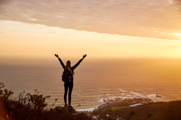 Fototapeta premium Rear View Of Active Young Woman Hiking Along Coastal Path At Sunset With Arms Outstretched