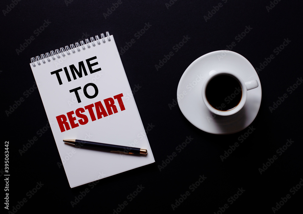 Poster time to restart is written in a white notebook in red type near a white cup of coffee on a black tab