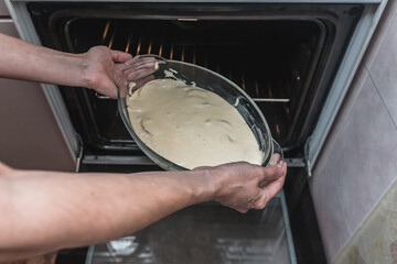 Process of cooking delicious homemade apple pie by grandma recipe. Female hands setting bakeware with raw dough into oven