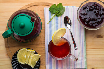 Berry tea in a cup next to lemon, honey, lemon balm, ginger and a teapot on the table on a round...