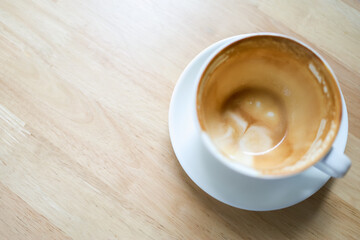 Closeup of empty dirty white cup of hot coffee latte with milk foam on wooden table.