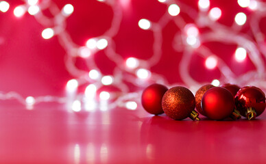 Toy Christmas balls of red color lie on a red background. Christmas garland in the background