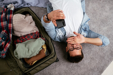 Young smiling man packing clothes into travel bag. Man preparing for the trip