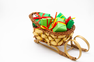 Old-fashioned wicker Santa sleigh with Christmas gifts wrapped in green paper with red ribbon