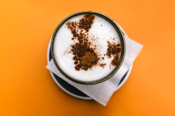 Cup of cappuccino with cocoa on an orange background.