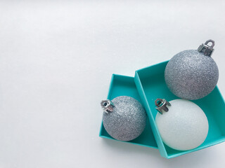 Turquoise jewel boxes inside of which is a shiny Christmas balls white and silver color on the right. White background. Copy space