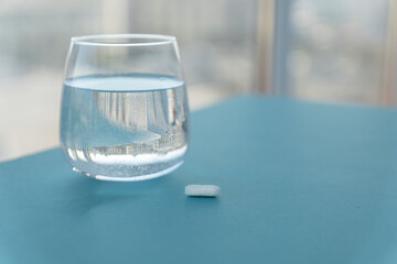 transpatent round glass of pure water and white pill on blue table, copy space for text. Treatment from headaches, flu, influenza, viruses. Healthcare concept