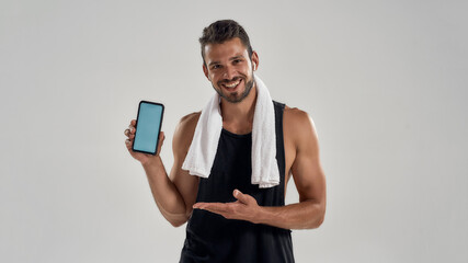 Happy young caucasian bodybuilder demonstrating smartphone with active screen