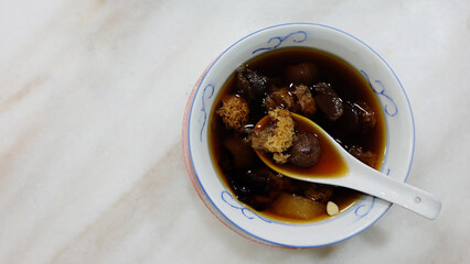 Chinese white fungus and longan sweet soup, in a bowl with Chinese soup spoon, placed on a marble table. Top view.