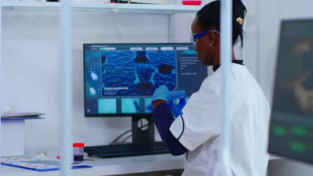 African chemist nurse writing on computer analysis results in modern equipped laboratory. Multiethnic doctors examining vaccine evolution using high tech researching diagnosis against covid19 virus