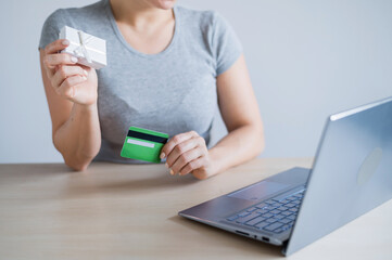 A faceless woman holds a gift box and a credit card in her hands while sitting at a laptop. The girl buys gifts online