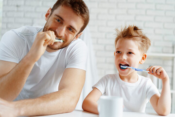 Dad and little son brushing teeth together