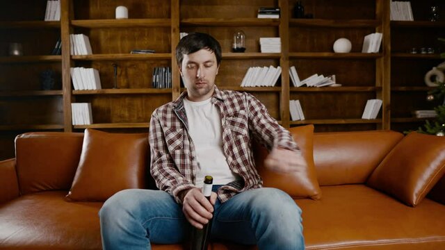 Alcohol addiction at young age. Caucasian male cannot stop drinking alcohol, drunken lonely male drinks wine from bottle. Loneliness, depression and alcoholism during Christmas and New Year holidays