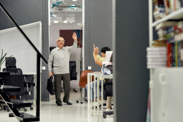 Full length shot of cheerful aged man, senior intern saying goodbye to his young colleagues while...